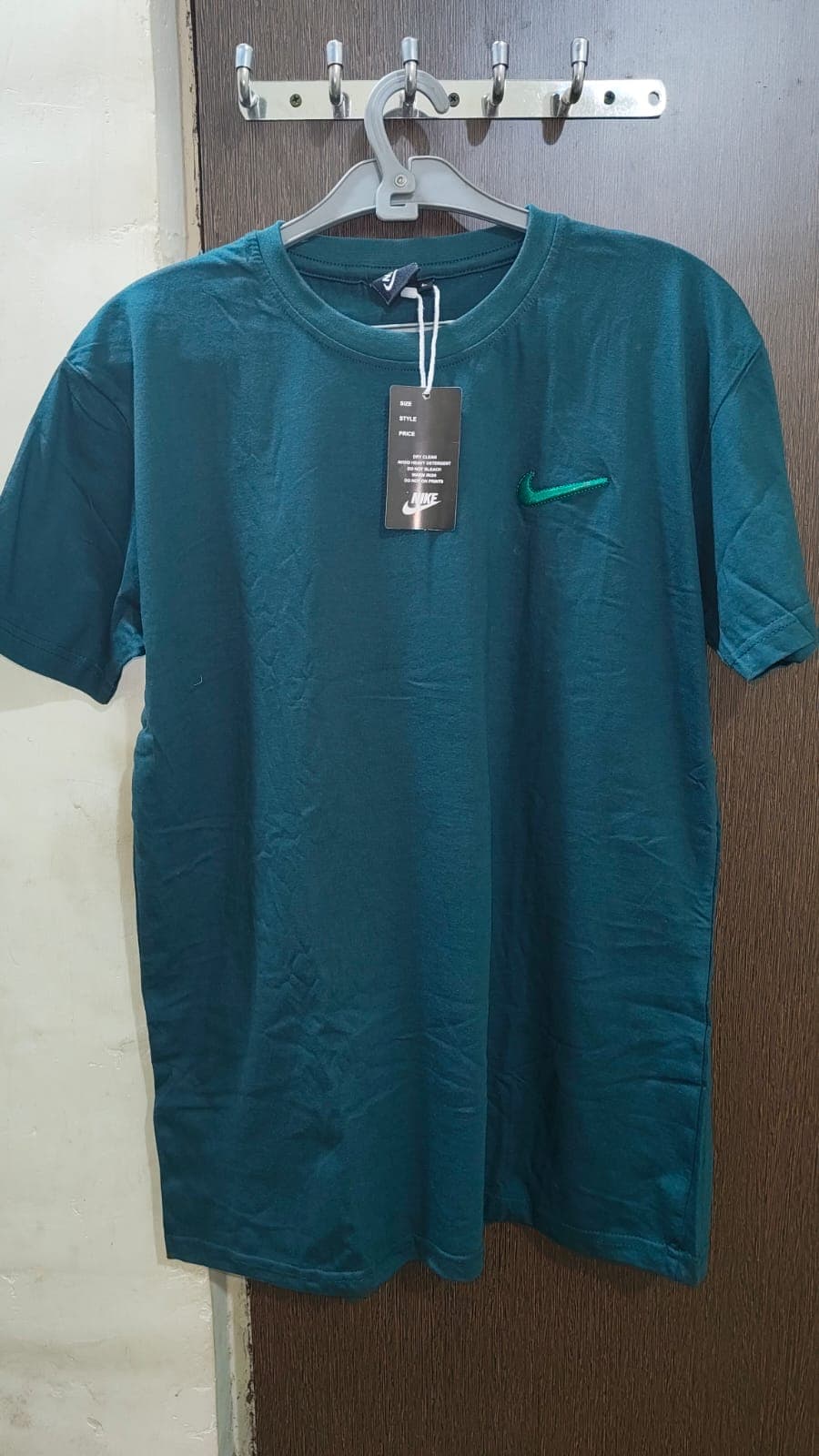 हैंगर पर टंगी गहरे हरे रंग की नाइकी टी-शर्ट, हरे लोगो और टैग के साथ।