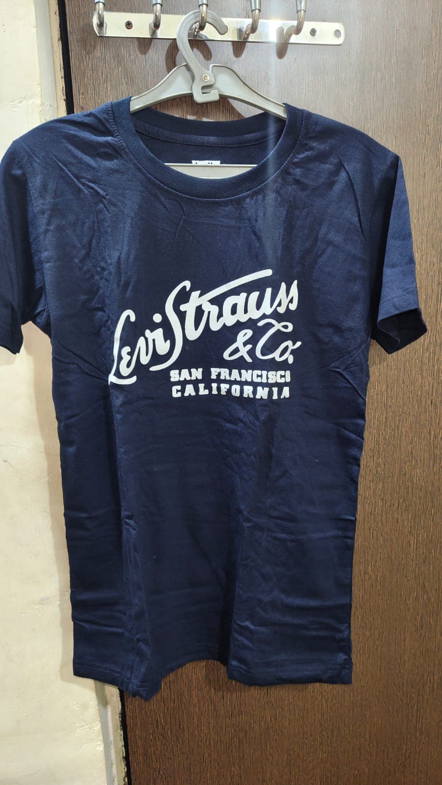 ग्रे हैंगर पर लटकी सफेद प्रिंट वाली नेवी ब्लू लेवी स्ट्रॉस एंड कंपनी की टी-शर्ट।