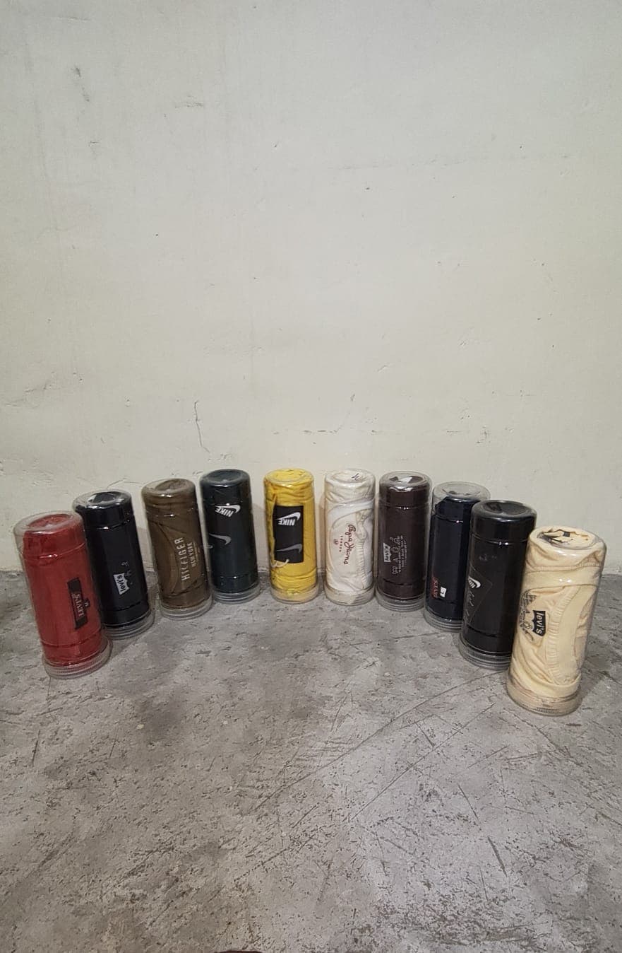 पारदर्शी कंटेनरों में लिपटी विभिन्न ब्रांडों की रंगीन टी-शर्ट, फर्श पर अर्धवृत्त में व्यवस्थित।